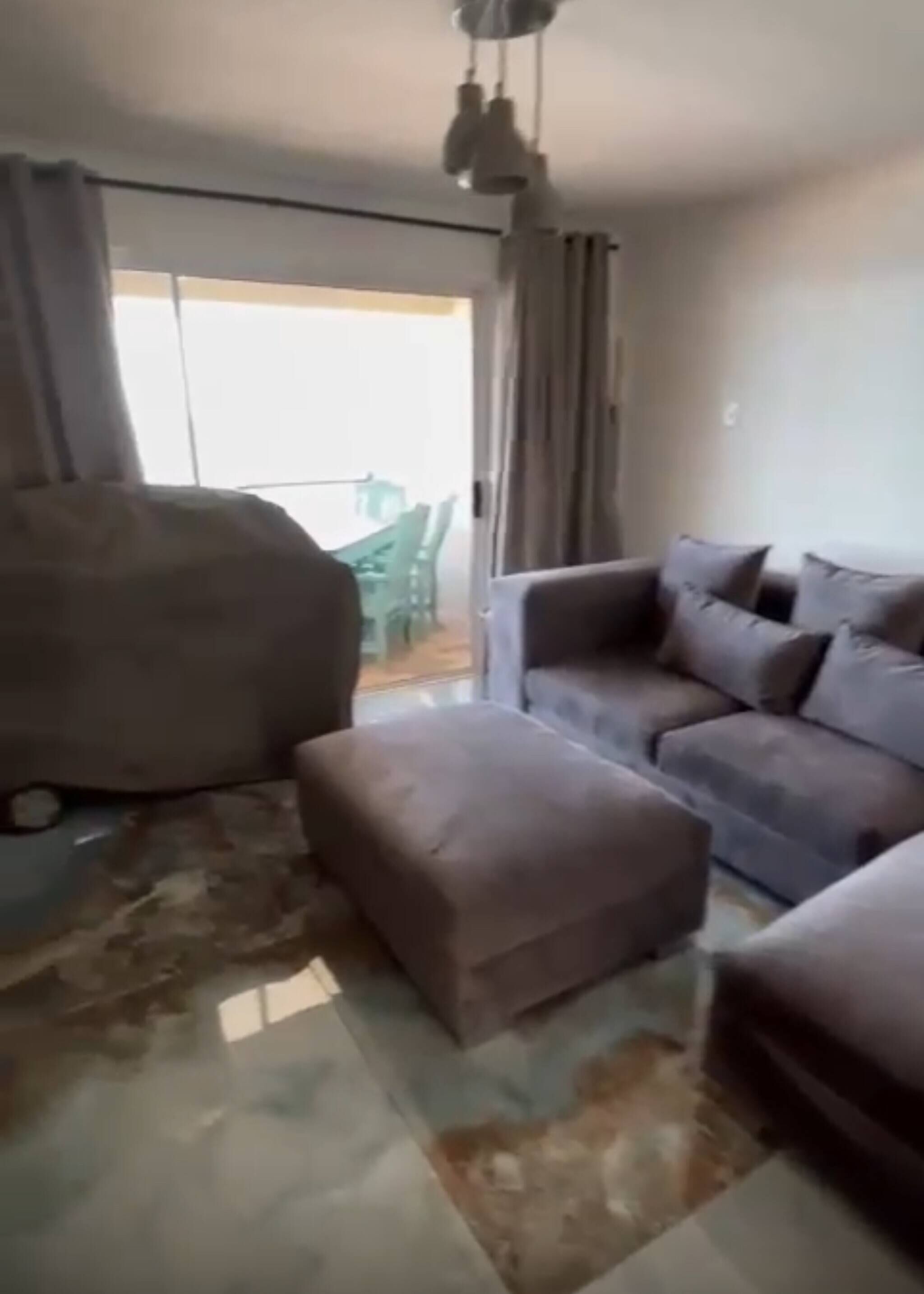 A living room with a sofa, ottoman, and a large bean bag chair. There is a sliding glass door leading to an outdoor area.