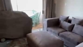 A living room with a sofa, ottoman, and a large bean bag chair. There is a sliding glass door leading to an outdoor area.