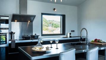 A modern kitchen with a large window, stainless steel appliances, and a central island with glasses and a decorative bowl.