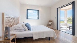 Quarto com cama, cadeira, janela e varanda com vista.
