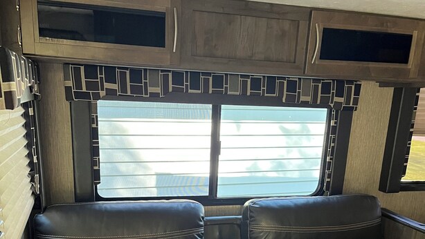 A black leather sofa with a center console, a window with blinds, and wooden paneling above.