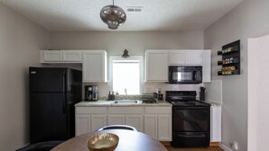 A modern kitchen with white cabinetry, a black refrigerator, a microwave, and an oven. There is a dining table with a bowl on it. - The Coziest Home Base in the Twin Cities (Crystal City)