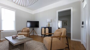 A living room with a flat-screen TV, two armchairs, a coffee table, and a lamp. - The Coziest Home Base in the Twin Cities (Crystal City)