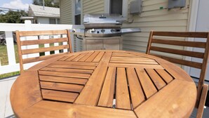 A wooden table with four chairs, a barbecue grill, and a white fence. - The Coziest Home Base in the Twin Cities (Crystal City)