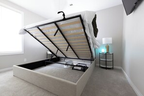A compact bed with a storage drawer underneath, a bedside table with a lamp, and a window providing natural light.