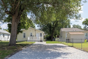 A residential area with a gravel driveway leading to a house with a porch.