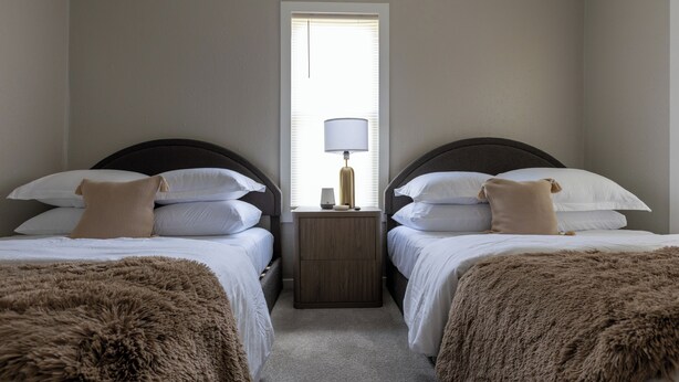 A twin room with two beds, a nightstand, a lamp, and a window. - The Coziest Home Base in the Twin Cities (Crystal City)