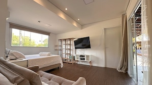 Habitación de hotel moderna con una cama grande, un sofá, un televisor montado en la pared y un ventanal con vistas a zonas verdes.