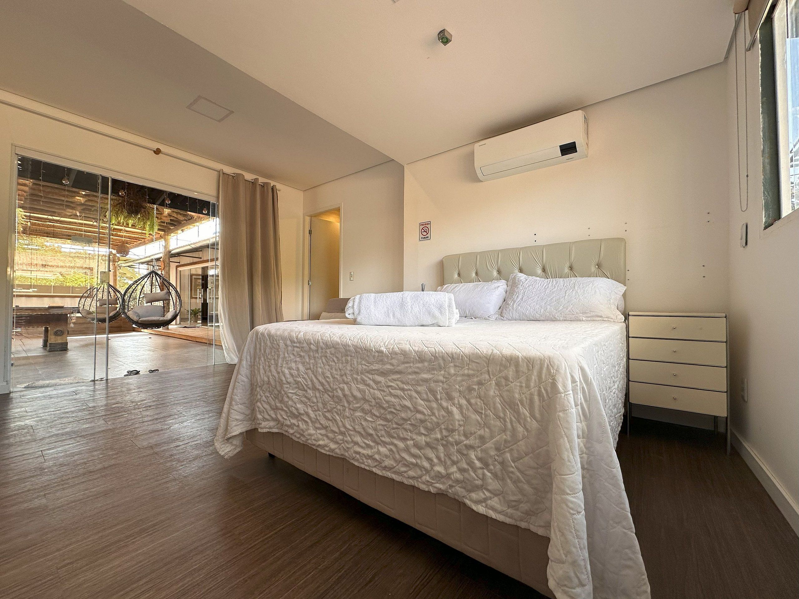 A bedroom with a bed, a bedside table, a nightstand, a window, and a view of an outdoor area.