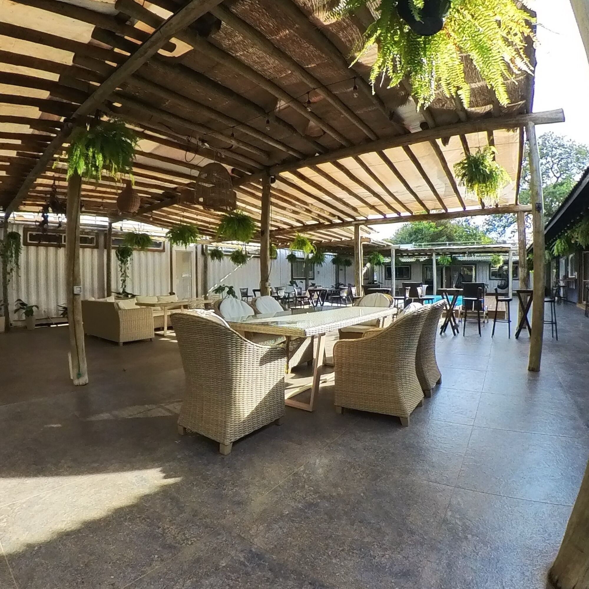 Un patio exterior con mobiliario de mimbre, una piscina y plantas colgantes.