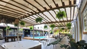 Un espacio exterior techado con jacuzzi, asientos y plantas en macetas.