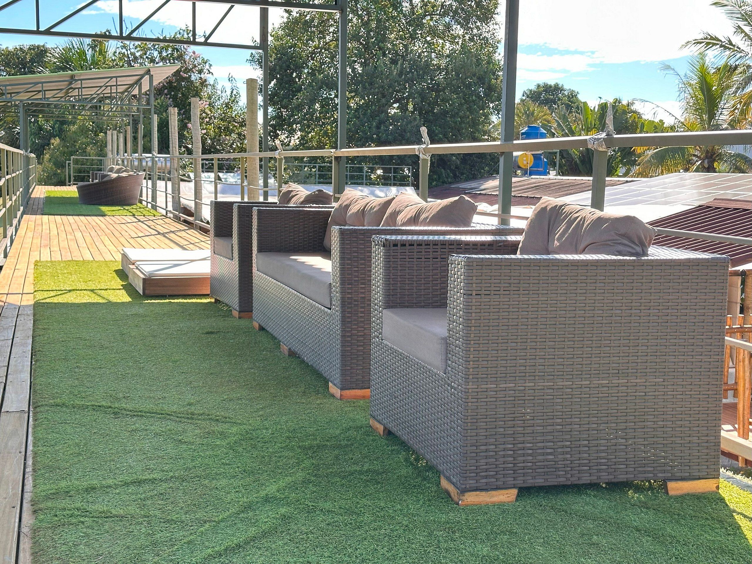 Sofás de vime ao ar livre com almofadas, dispostos num deck de madeira com grama artificial.