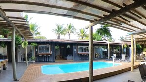 Ein überdachter Außenbereich mit Pool, Sitzgelegenheiten und einem Gebäude mit einem Ziegeldach.