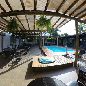 A covered outdoor area with a pool, wooden furniture, and potted plants.