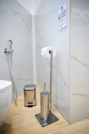 A bathroom with a toilet, a paper towel dispenser, a trash bin, and a shower. - A stylish and cozy studio apartment, equipped with all the amenities. (Torre del Greco)
