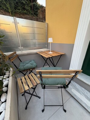Eine Terrasse mit einer Holzbank, zwei kleinen Tischen und einem grünen Kissen.