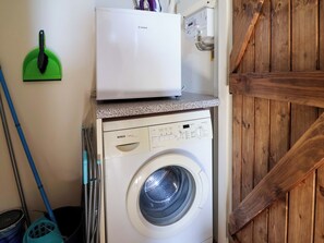 Une machine à laver avec un panneau de commande, une pelle à poussière verte et une serpillière appuyée contre le mur.