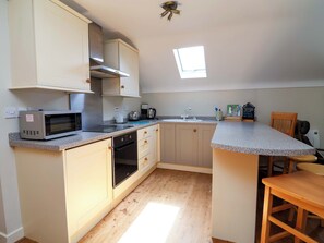 Eine kompakte Küche mit Mikrowelle, Backofen und Spüle. Ein kleines Fenster sorgt für natürliches Licht, und es gibt einen Holztisch.