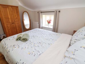 Une chambre à coucher avec un lit, une armoire en bois, un miroir, une fenêtre avec des rideaux et un radiateur.