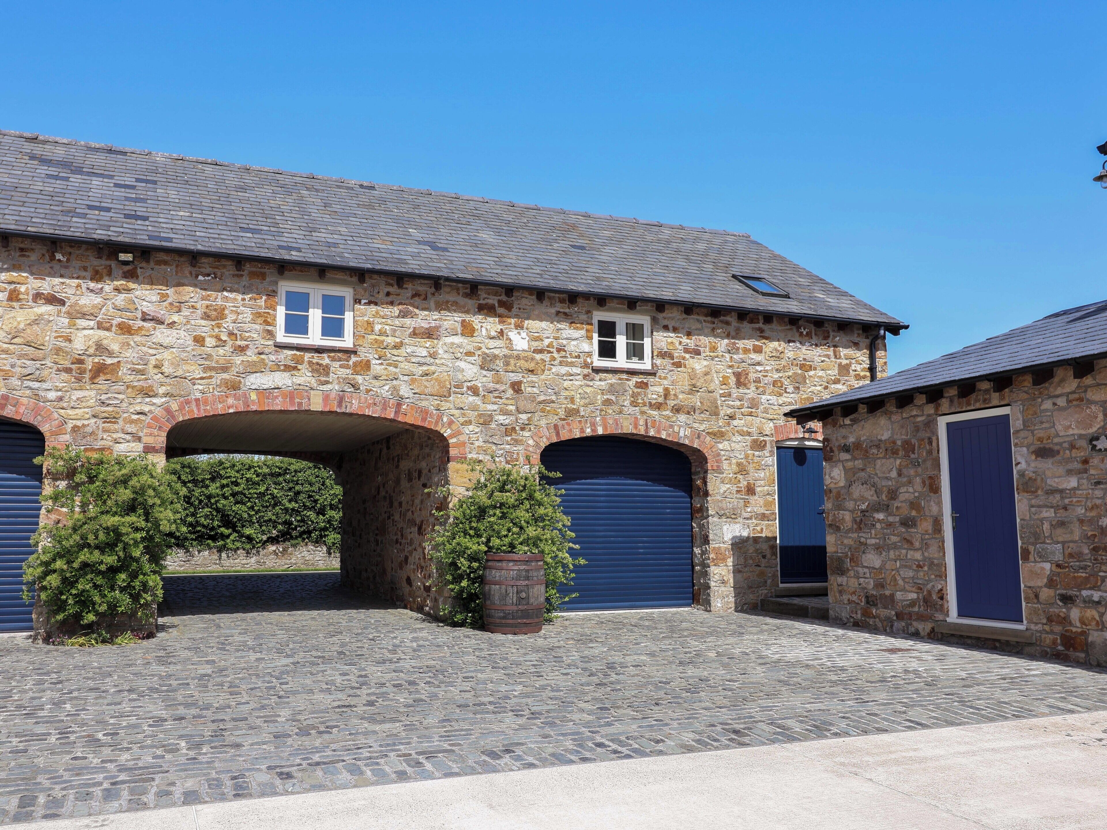 A stone building with a covered entrance, two blue garage doors, and a paved courtyard.