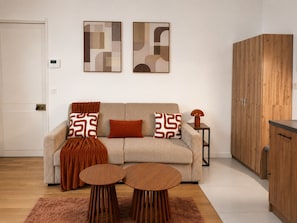 Een moderne woonkamer met een bank, twee bijzettafels, een houten kast en abstracte wanddecoratie.