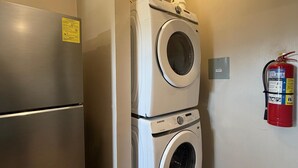 Ein kleiner Waschraum mit einem Edelstahlkühlschrank und gestapelten Waschmaschinen.