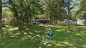 A residential area with a house surrounded by trees, a covered porch, and a grassy yard. - Sacandaga Lake Retreat w/dock & Screened In Porch (Northville)