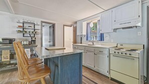 A kitchen with white cabinets, a stove, a sink, and a dining area with wooden chairs. - Sacandaga Lake Retreat w/dock & Screened In Porch (Northville)