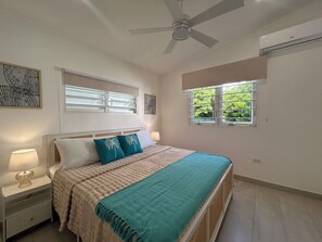 Ein Schlafzimmer mit einem Bett, einem Deckenventilator, einem Fenster mit Jalousien und einer Klimaanlage.