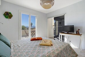 A bedroom with a bed, a TV, a desk, and a view of the outdoors.