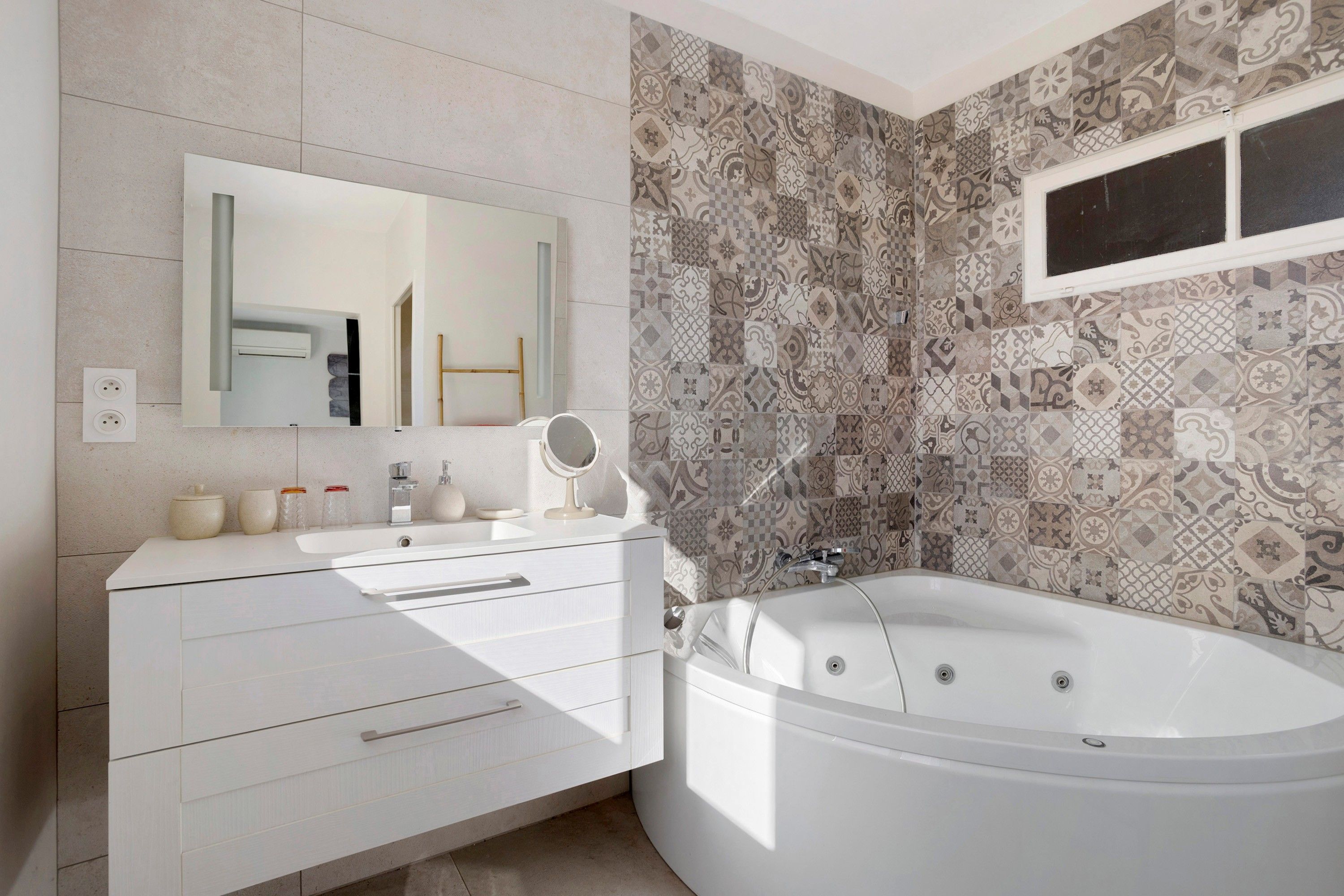Une salle de bain moderne avec une baignoire sur pieds, un meuble-lavabo avec un miroir et des carreaux décoratifs sur les murs.