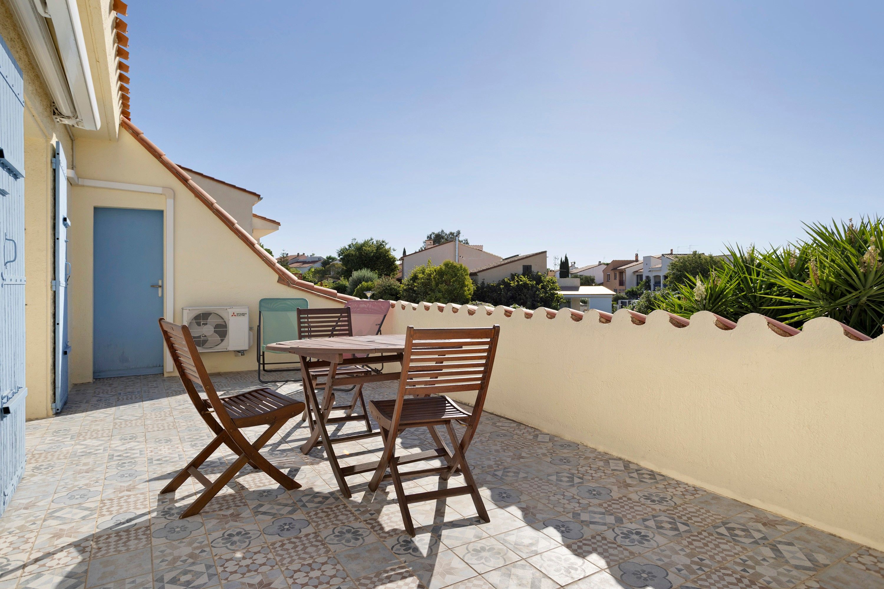 Un patio con una mesa, sillas, una puerta y un muro con detalles decorativos.