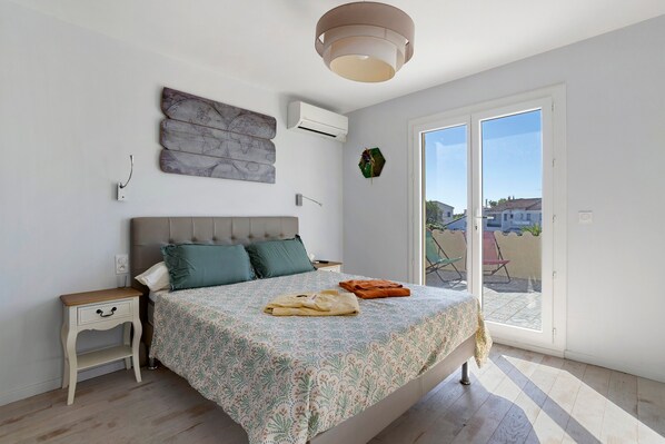 A bedroom with a bed, a nightstand, a wall-mounted air conditioner, a globe artwork, and a view through a sliding door.