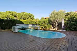A swimming pool with a wooden deck, surrounded by greenery and trees.