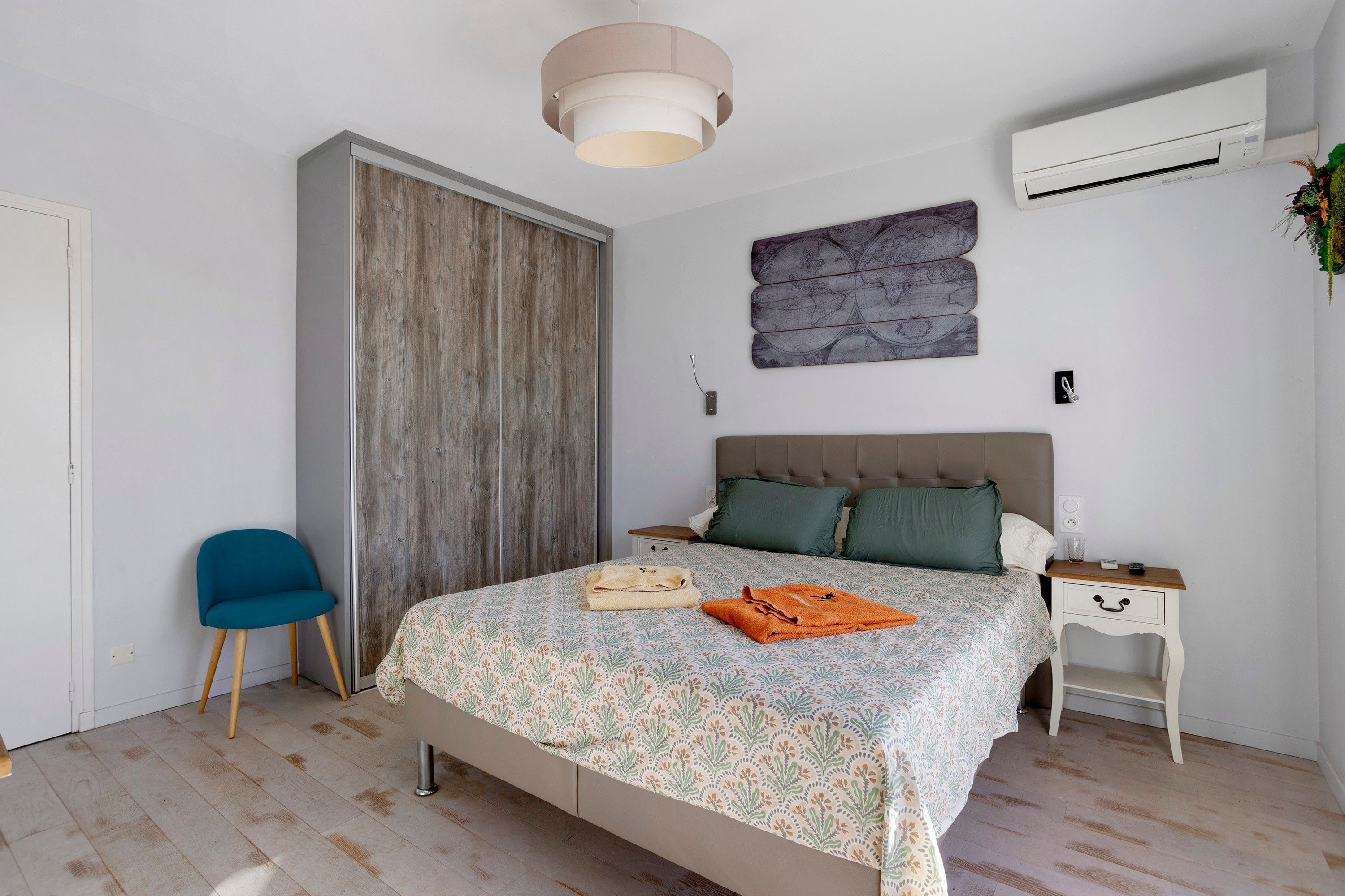 Ein Schlafzimmer mit einem Bett, einem Sessel, einem Kleiderschrank, einem Nachttisch und einer Klimaanlage.