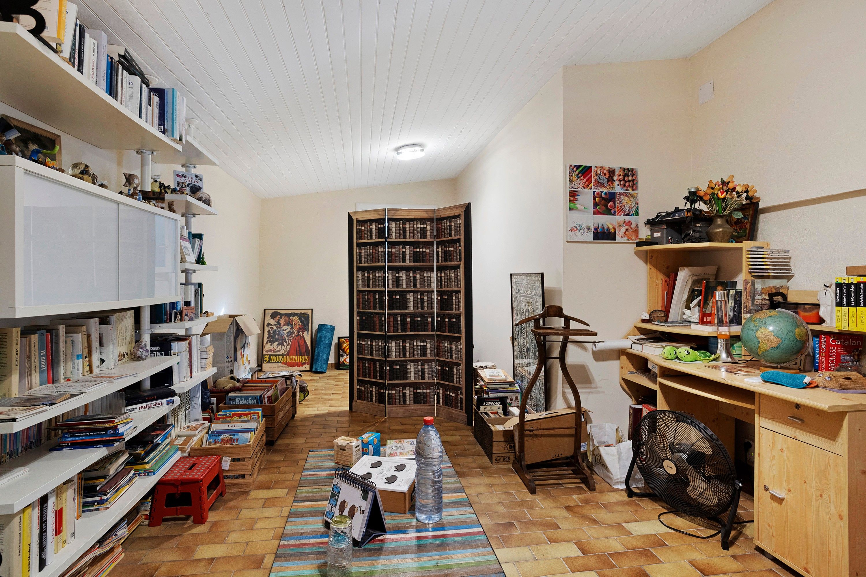 Una habitación con una amplia estantería, un escritorio con un globo terráqueo y libros, y una silla.