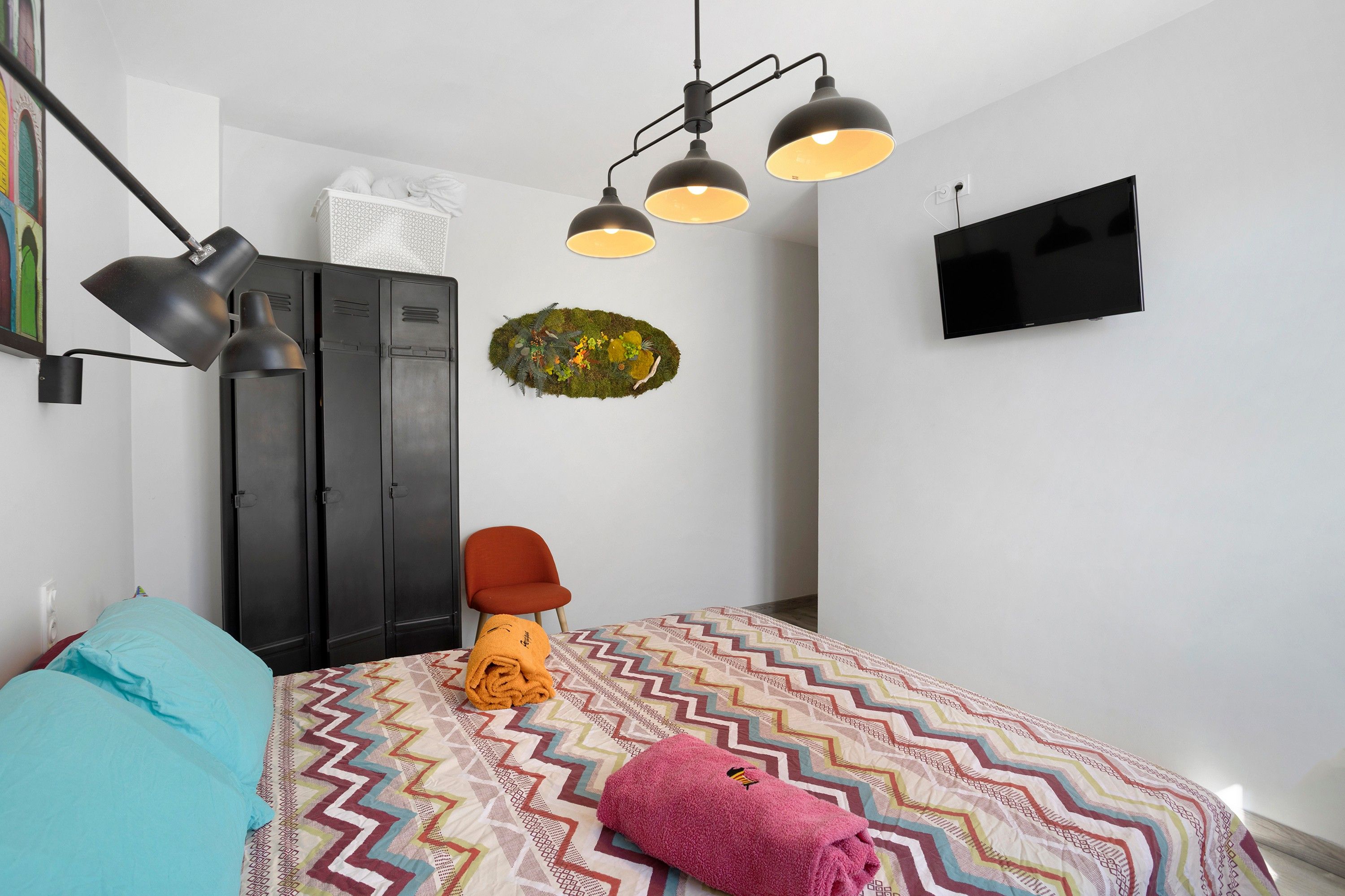 Ein Schlafzimmer mit einem Bett, einem Kleiderschrank, einem Fernseher und einer Wandleuchte.