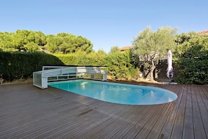 Una piscina con plataforma de madera, rodeada de follaje y árboles.