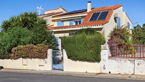 Un edificio residencial con una turbina eólica, paneles solares y un acceso con portón.