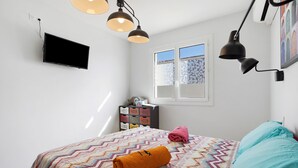 Un dormitorio con cama, dos lámparas de pared, un televisor, un ventanal con vistas y un aparador con cajas de almacenamiento.