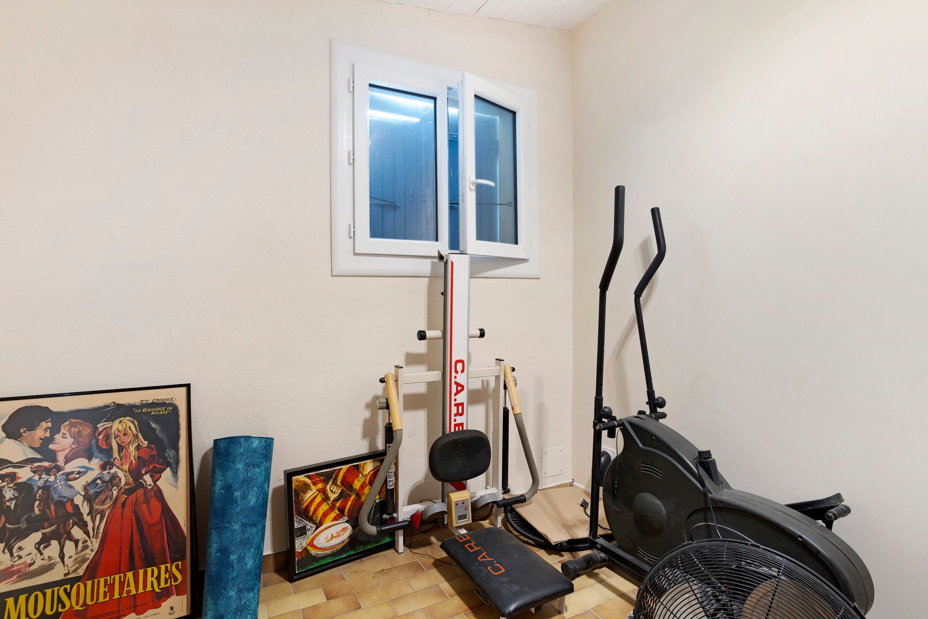 Een huisgymnasium met fitnessapparatuur, een raam en een poster aan de muur.