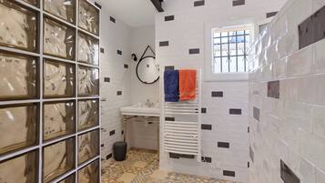 A bathroom with a white sink, a mirror, a towel rack with two towels, patterned floor tiles, and a window with bars.