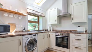 A compact kitchen with a washing machine, oven, microwave, and a window with a view. - Ty Haf (Mold)