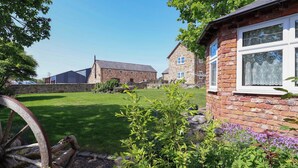 A stone building with a brick extension, a grassy yard, and a wooden wheel. - Ty Haf (Mold)