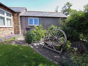 Ein rustikaler Hollschuppen mit Fenster und einer Schubkarre im Garten.