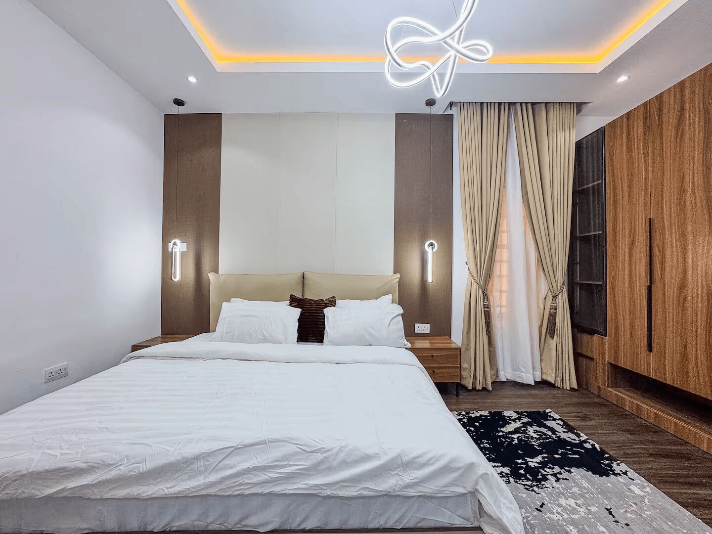Un dormitorio moderno con una cama, mesitas de noche, lámpara de pared, ventana con cortinas y un armario de madera.