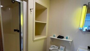 Et badeværelse med toilet, vask, bruseniche og en hylde over toilettet.