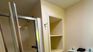 Et badeværelse med toilet, bruseniche og en hylde med toiletartikler.