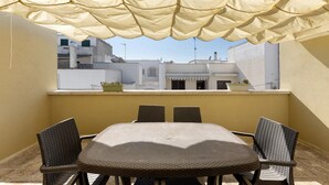 A balcony with a table and chairs, a beige canopy, and a view of buildings in the background. - Apartment 'La Putea Salento' with Private Terrace, Wi-Fi and Air Conditioning (Corsano)