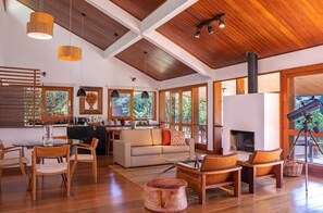 A spacious living area with a high ceiling, wooden beams, a fireplace, and large windows offering a view of the outdoors. - Pousada do Cedro (Santo Antônio do Pinhal)